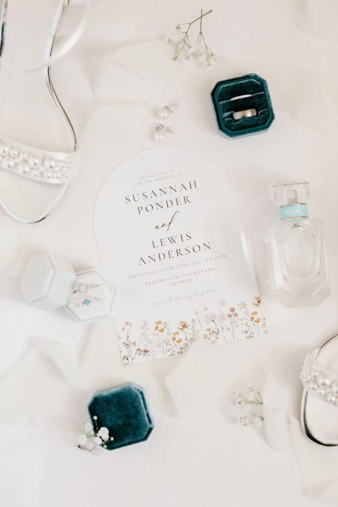 Wedding invitation and stationery flat lay with perfume and jewellery details.
