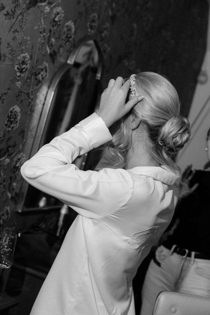 Bride adjusting her hair in the mirror during quiet wedding morning moments.