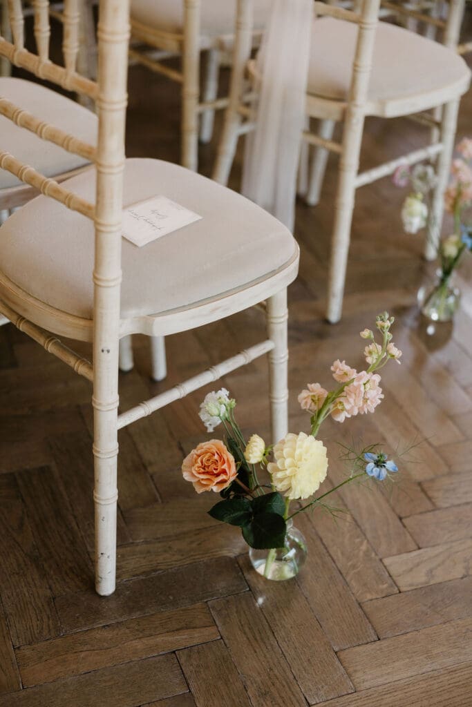 Wedding ceremony chair detail with single stem flowers tied to white wooden chairs at Broxmouth Courtyard.