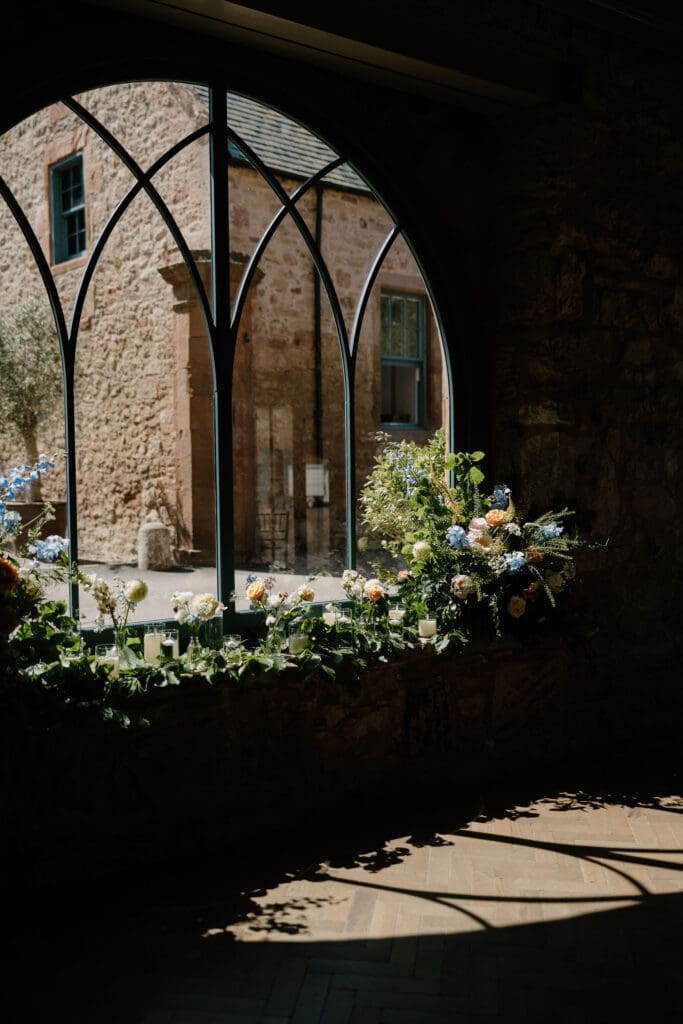 View through the arched stone window at Broxmouth Courtyard during a wedding ceremony.