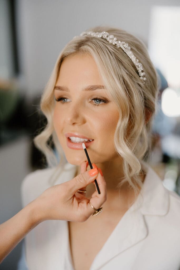 Bride having final makeup touches applied during relaxed wedding morning prep.