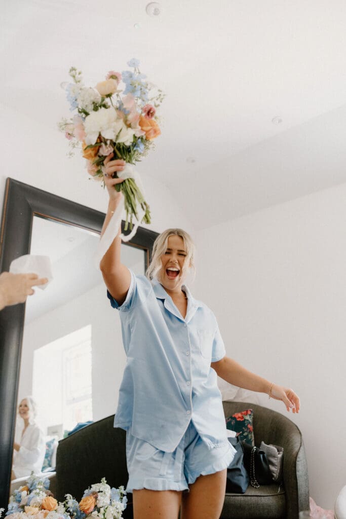 Bridesmaid celebrating with friends in blue pyjamas during wedding morning preparations.