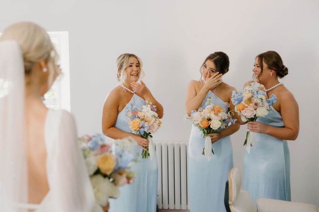 Bridesmaids reacting emotionally while holding bouquets during wedding morning.