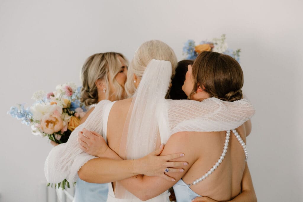 Bride sharing a group hug with bridesmaids before the ceremony.