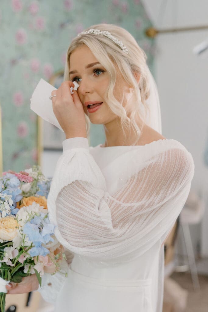 Bride wiping away happy tears while holding her bouquet during morning prep.