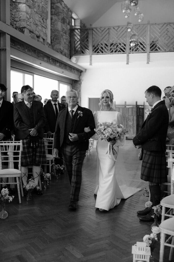 Bride and dad walking down the aisle inside Broxmouth Courtyard, photographed in black and white.