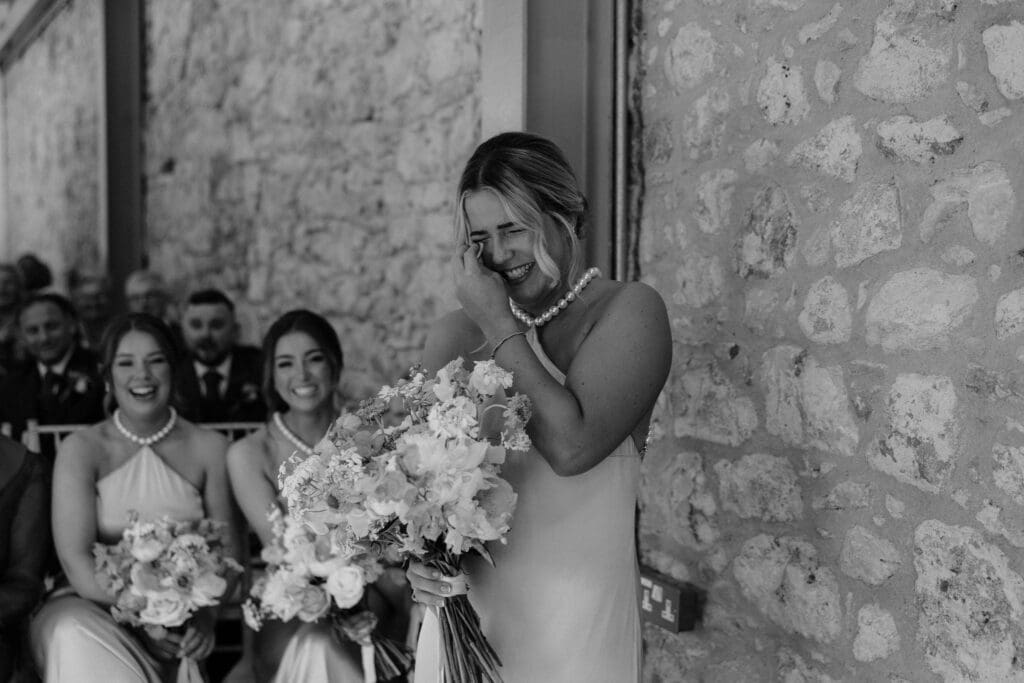 Bridesmaid laughing through happy tears while holding her bouquet during the ceremony.