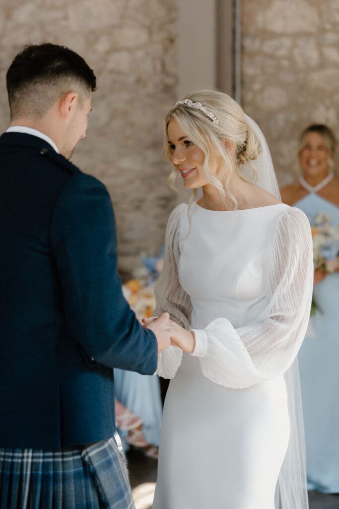 Bride and groom holding hands and smiling during their vows inside Broxmouth Courtyard.