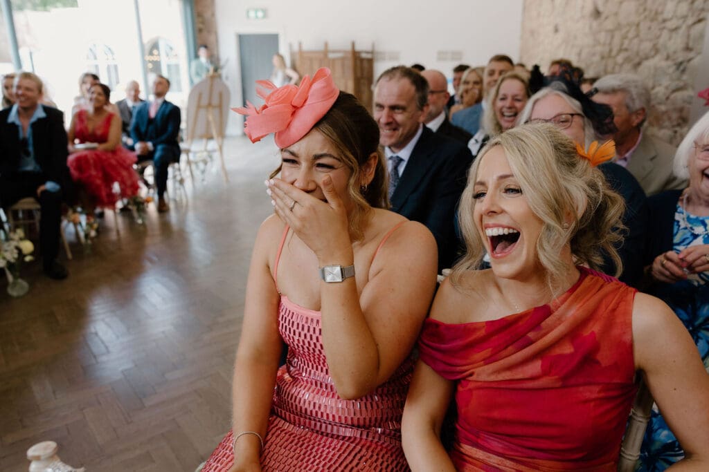 Wedding guests laughing during the ceremony, captured candidly inside Broxmouth Courtyard.