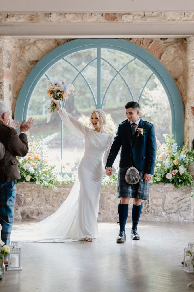 Bride and groom celebrating at the end of their ceremony beneath the arched window.