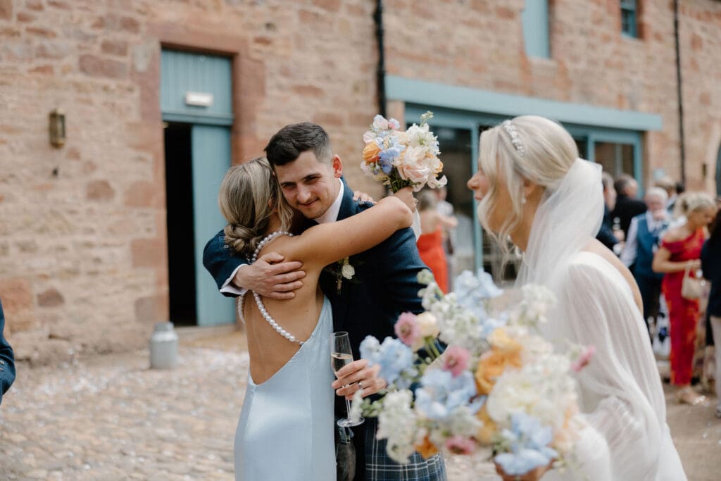 Bridesmaid hugging groom during the outdoor wedding celebration at Broxmouth Courtyard